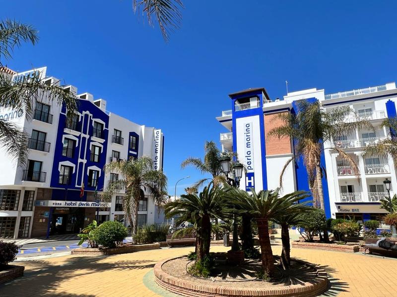 Mehrstöckige Gebäude mit weiß-blauen Fassaden um einen Innenhof mit Palmen unter blauem Himmel.