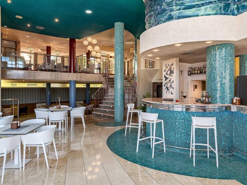 Moderner Café-Innenraum mit türkisfarbenem Tresen, weißen Stühlen und zweistöckigem Design.