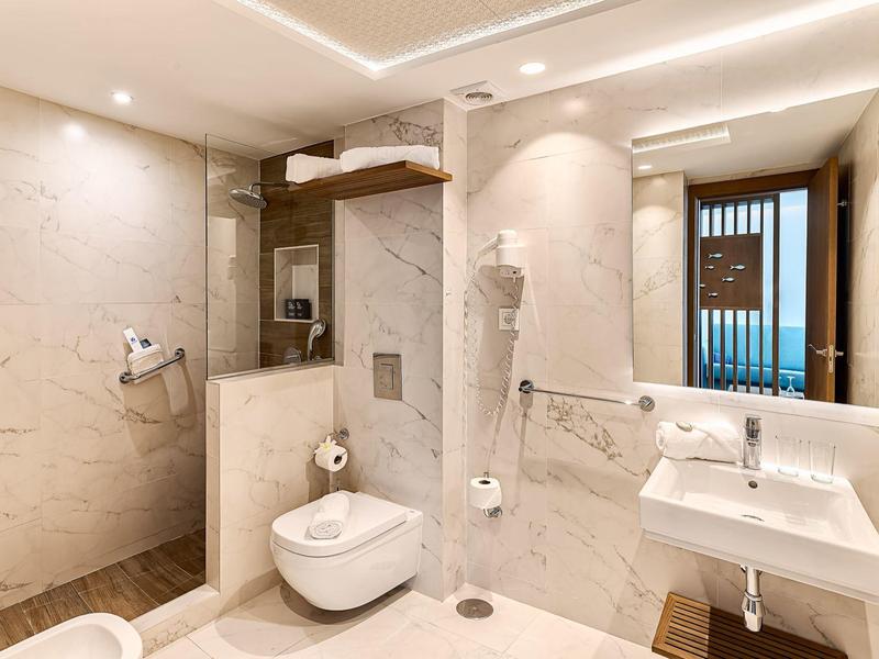 Helles Badezimmer mit weißem Marmor, Glasdusche, wandhängendem WC, großem Spiegel und Waschbecken.