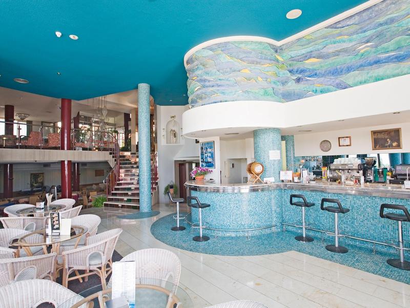 Moderner Cafébereich mit blauem Tresen, weißen Stühlen und Treppe zur Galerie im Hintergrund.