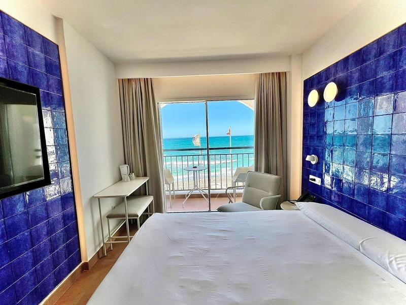 Helles Schlafzimmer mit blau gekachelter Wand, großem Bett und Meerblick durch Balkontür.