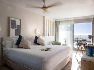 Hell eingerichtetes Schlafzimmer mit großem Bett, Balkon und Meerblick bei Tageslicht.