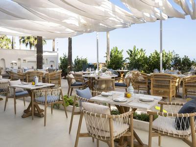 Offener Terrassenbereich eines Hotels mit vielen Tischen, Stühlen und Pflanzen in modernem Stil.