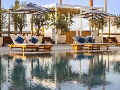 Luxuriöser Poolbereich mit Liegen, blauen Kissen und großen Sonnenschirmen an sonnigem Tag.