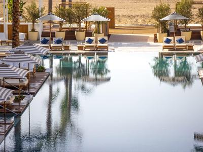 Einladender Pool mit Liegestühlen und Sonnenschirmen, umgeben von Bäumen und Sandboden.