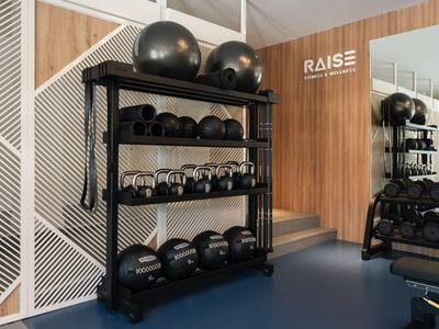 Gym mit Hanteln und Kettlebells auf einem schwarzen Regal vor Holzwand und Spiegel.