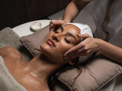 Frau entspannt auf Massagebank, während Hände sanft Stirn und Gesicht massieren.