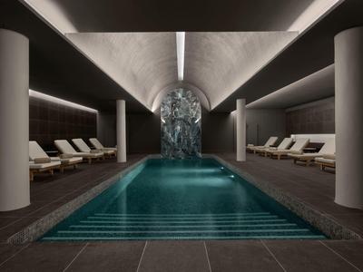 Innenpool in modernem Raum mit hellen Säulen, Liegestühlen und Wasserfall-Farbspiel am Ende.