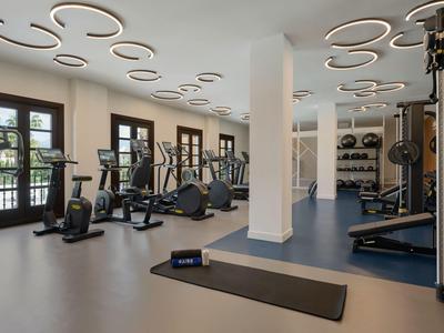 Moderner Fitnessraum mit Fahrrädern, Laufbändern und Hanteln in hellem Raum mit runden Deckenleuchten.