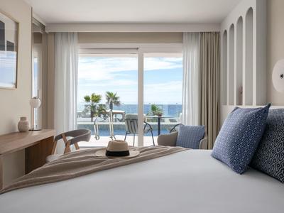 Helles Schlafzimmer mit Doppelbett, blauen Kissen, Holzmöbeln und Balkon mit Meerblick.