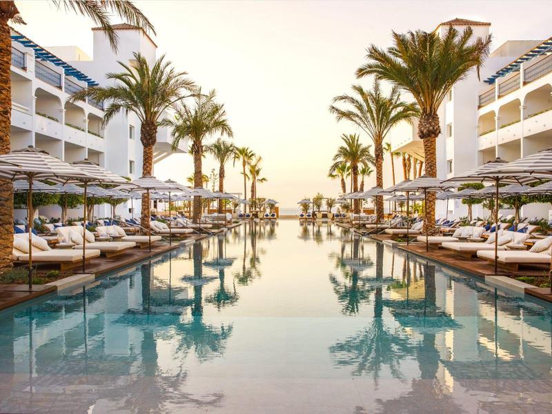 Moderner Hotelpool mit Palmen und Liegestühlen bei Sonnenuntergang.