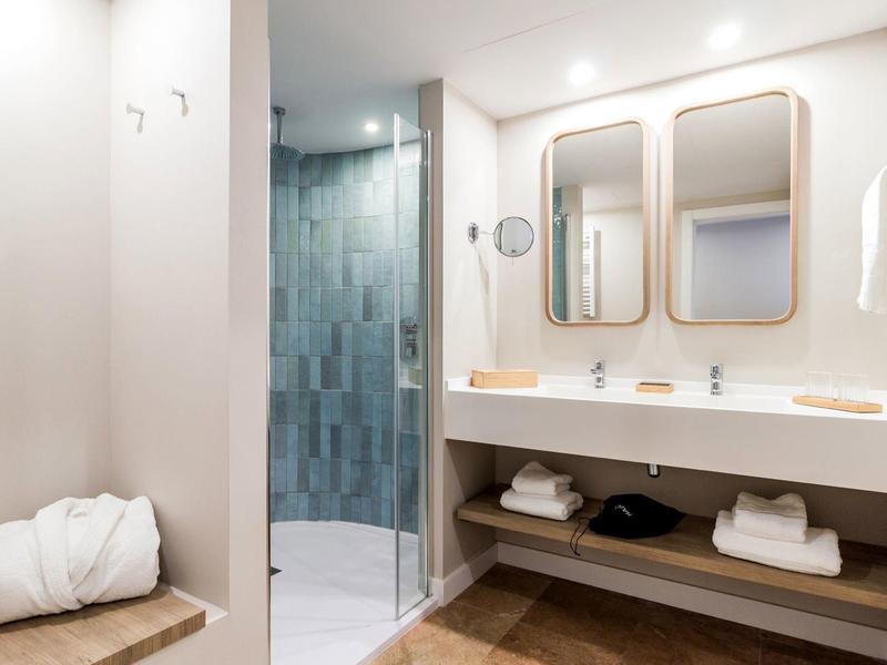 Modernes Badezimmer mit zwei Spiegeln, Doppelfußwaschbecken, Glasdusche und Handtüchern auf Holzbänken.