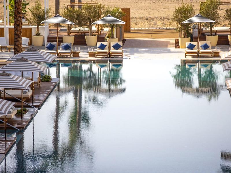 Einladender Pool mit Liegestühlen und Sonnenschirmen, umgeben von Bäumen und Sandboden.