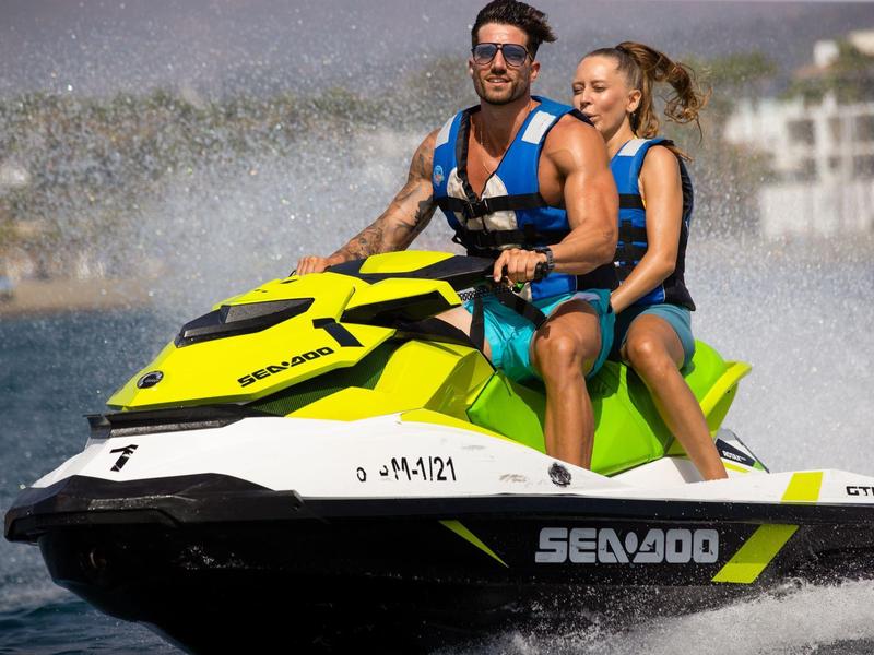 Zwei Personen fahren mit einem gelben und schwarzen Jetski auf ruhigem Wasser bei Sonnenschein.