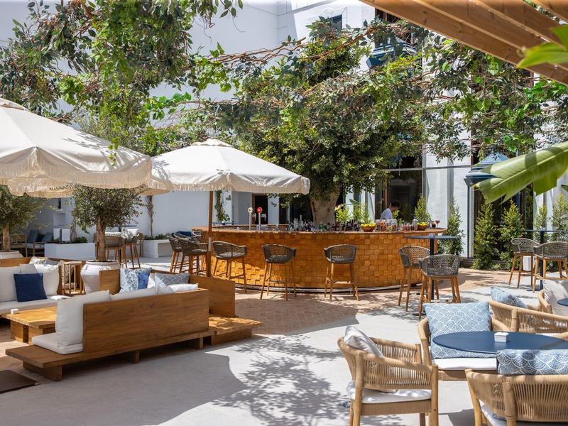 Moderner Außenbereich mit Holzmöbeln, Sonnenschirmen, Bar und grünen Pflanzen bei Tageslicht.