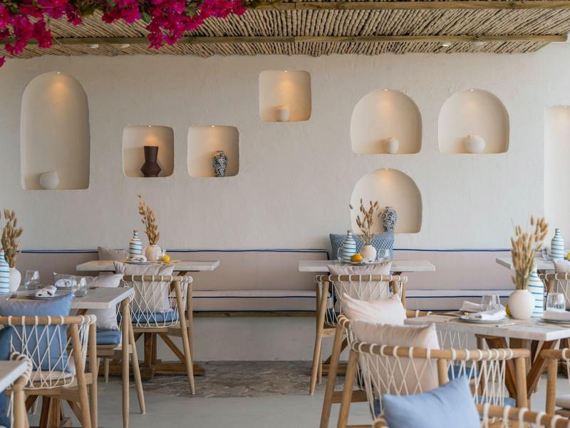 Helles Café mit Holzmöbeln, blauen Kissen, Wandnischen und Dekorationen aus Trockenblumen.