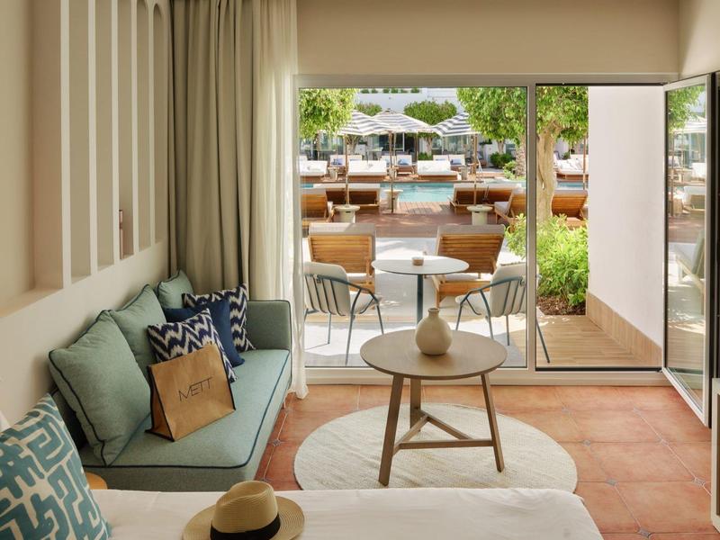 Helles Wohnzimmer mit Sofa, Kissen, Couchtisch und Blick auf Terrasse mit Stühlen und Sonnenschirmen.