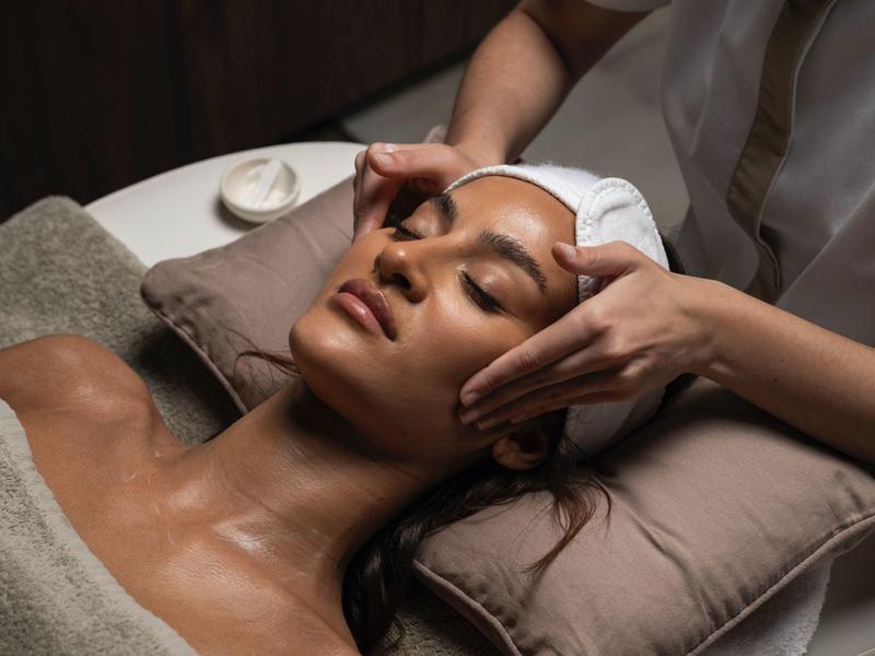 Frau entspannt auf Massagebank, während Hände sanft Stirn und Gesicht massieren.