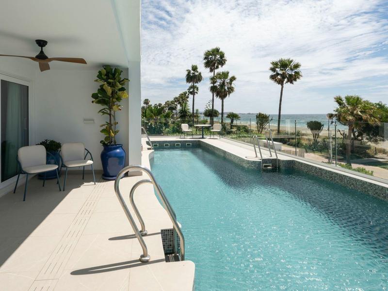 Moderner Pool mit klar blauem Wasser, Terrasse mit Sitzbereich und Blick auf Palmen und Meer.