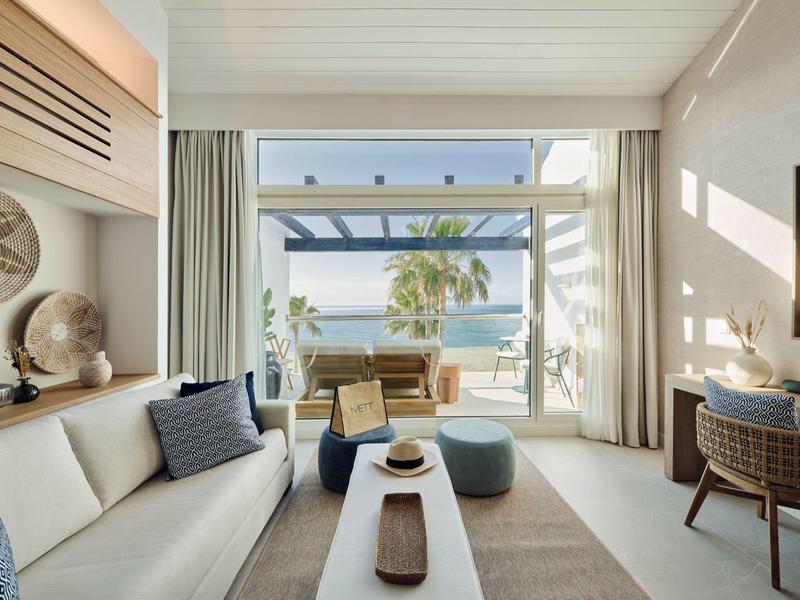 Heller Wohnraum mit Sofa, Couchtisch, Stühlen, großen Fenstern und Meerblick.