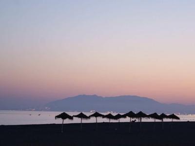 Sonnenuntergang am Strand mit dunkel silhouettierten Sonnenschirmen und ruhigem Meer.