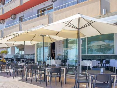 Area esterna dell'hotel con ombrelloni e tavoli davanti a finestre di vetro.