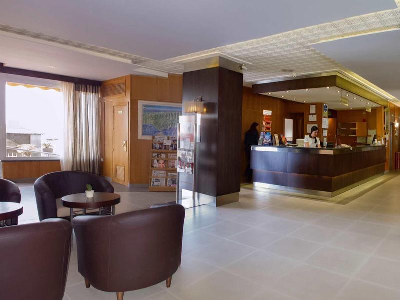 Helles Hotelzimmer mit Ledersesseln, Empfangstheke und großen Fenstern mit Ausblick.