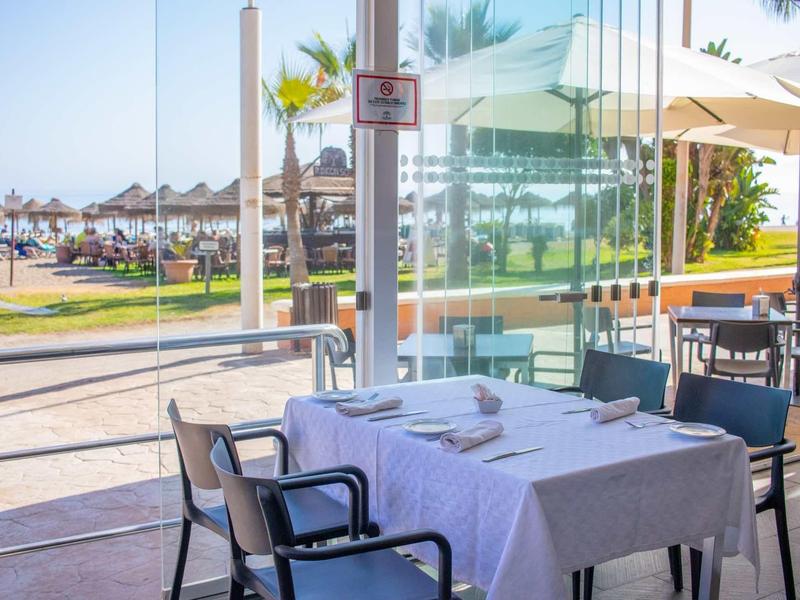 Ein gedeckter Tisch mit weißen Tischdecken und Stühlen auf einer sonnigen Terrasse am Meer.