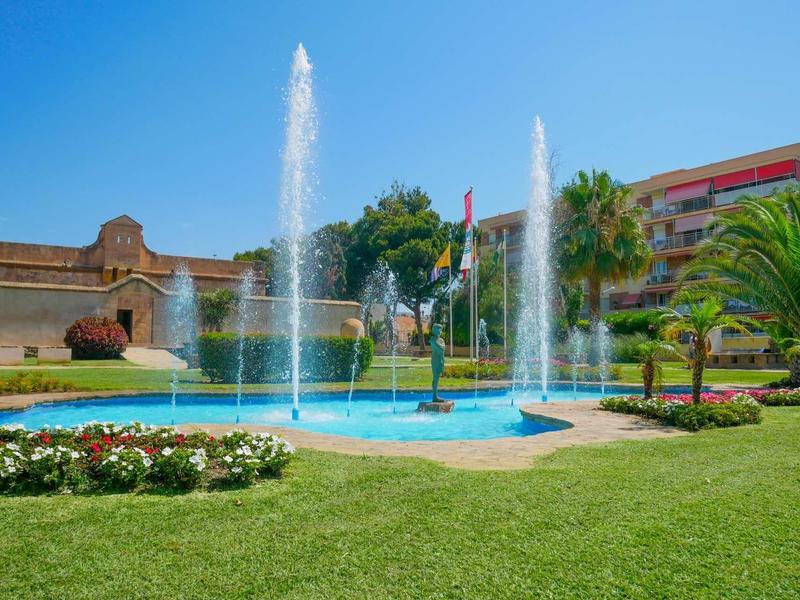 Schöner Park mit blauem Springbrunnen, grünen Palmen, bunten Blumen und klarem Himmel.