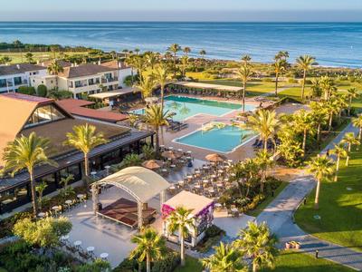 Ferienanlage mit Pool, grünen Gärten und Palmen an der Küste mit Blick auf das Meer.