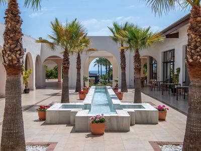 Innenhof eines Hotels mit Palmen und einem Wasserbecken unter blauem Himmel