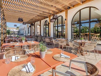 Gemütliche Außenterrasse eines Hotels mit Tischen, Stühlen und Sonnenschutz