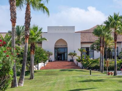 Modernes Hotelgebäude mit Palmen und gepflegtem Rasen unter blauem Himmel.