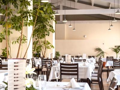 Eleganter Speisesaal mit weißen Tischdecken, Holzstühlen und grünen Pflanzen.