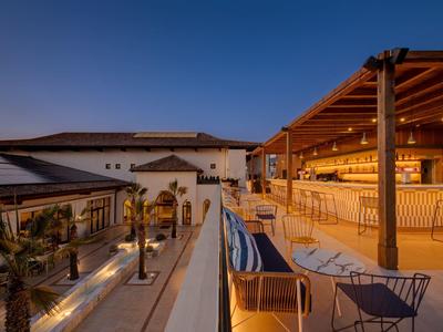 Moderne Hotelterrasse mit Bar, Stühlen und Abendbeleuchtung unter klarem Himmel.