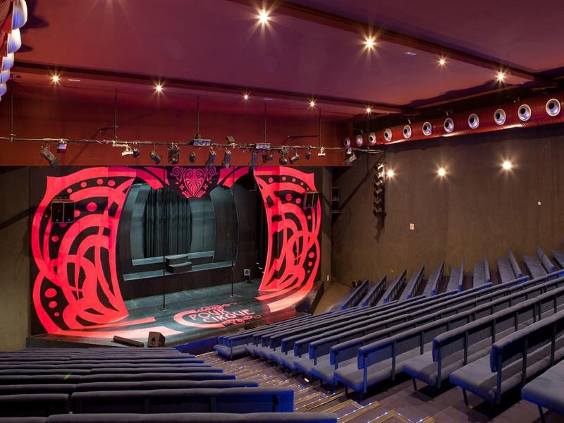 Innensicht eines Theaters mit roter, abstrakter Bühnenkulisse und blauen Sitzreihen.