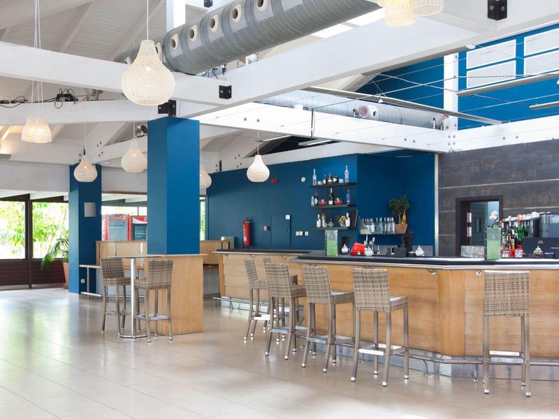 Moderner Hotelbarbereich mit blauen Wänden, Holzmobiliar und weißen Hängeleuchten.