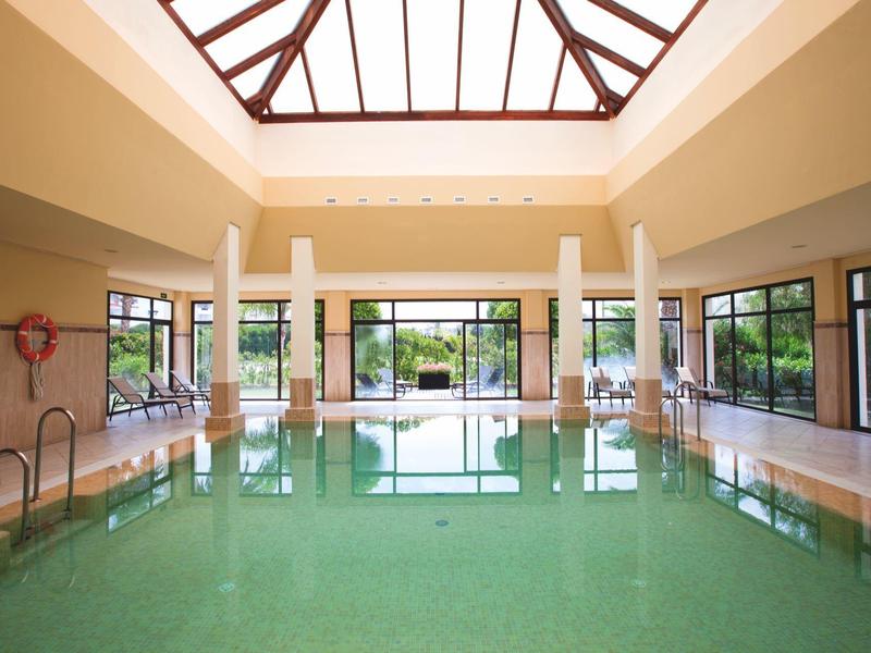 Großes Hallenbad mit Glasdach und Blick auf Garten durch große Fenster.