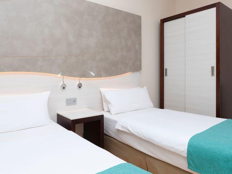 Zwei Einzelbetten mit weißen Bettlaken und türkisfarbenen Decken in einem Hotelzimmer mit Schrank und Nachttisch.