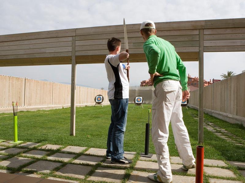 Zwei Männer üben Bogenschießen auf einem Außenstand mit Zielscheiben.