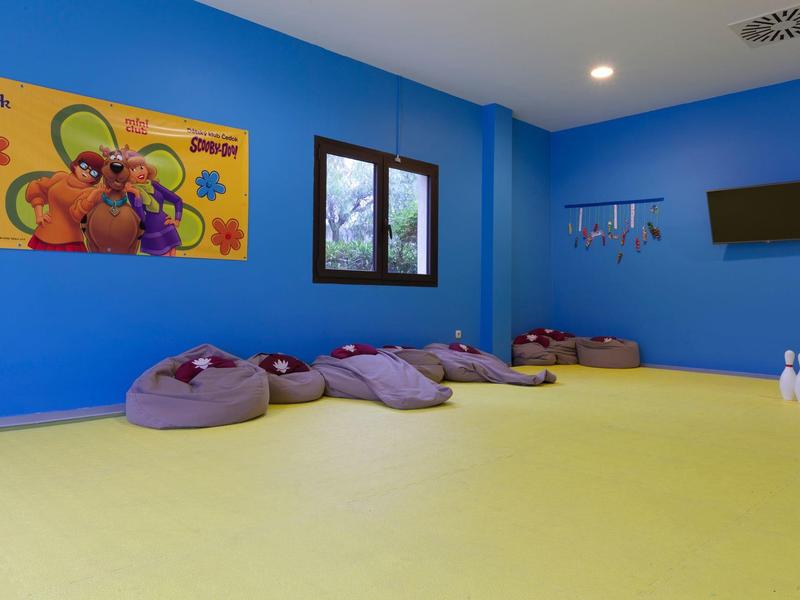 Ein heller, freundlicher Spielraum mit blauen Wänden, Sitzsäcken und einem Monitor an der Wand.