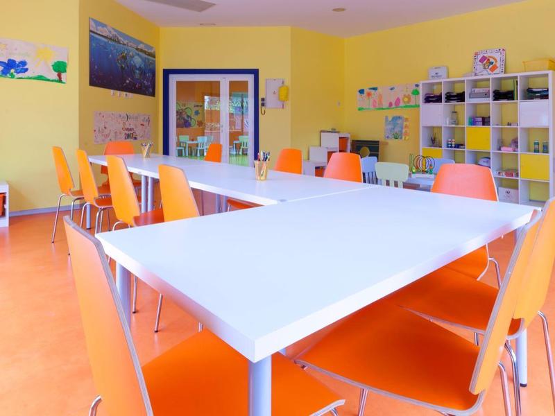 Heller, moderner Seminarraum mit weißen Tischen und orangefarbenen Stühlen vor gelben Wänden.