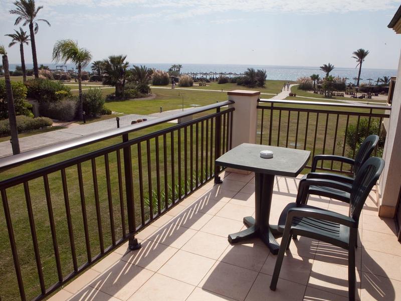 Balkon mit Tisch und zwei Stühlen mit Blick auf einen Garten und das Meer.