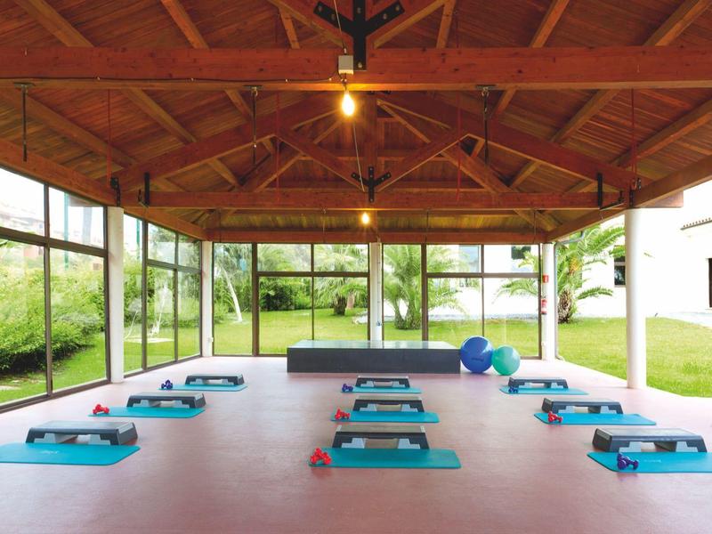 Heller Fitnessraum mit Holzdecke, großen Fenstern und blauen Yogamatten auf dem Boden.