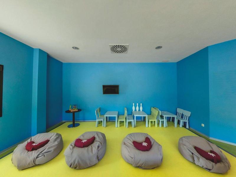 Bunter Spielraum mit blauen Wänden, gelbem Boden und Sitzsäcken vor kleinen Stühlen und Tischen