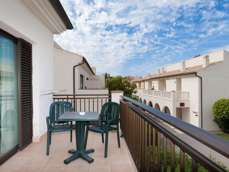 Balkon mit zwei Stühlen und kleinem Tisch in einem Hotel mit Blick auf benachbarte Gebäude.
