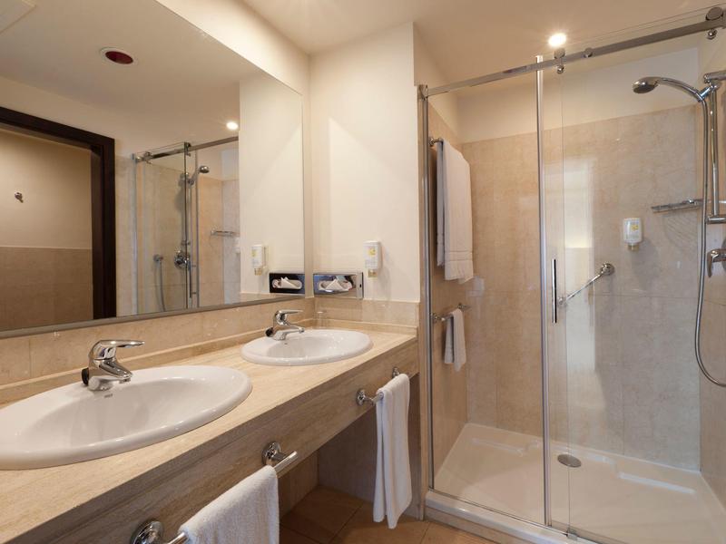 Helles Badezimmer mit Doppelwaschbecken und begehbarer Dusche mit Glaswand.