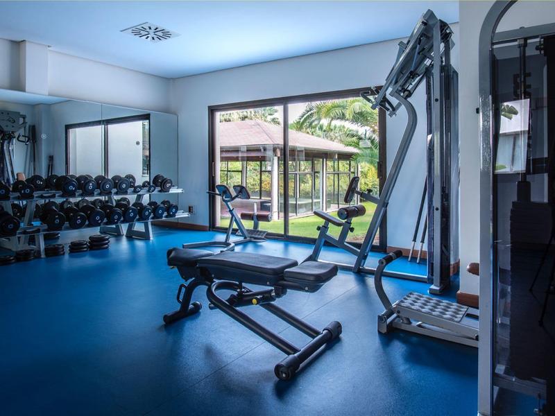 Moderner Fitnessraum mit Hanteln, Trainingsbank und Kabelzug vor großen Fenstern mit Blick ins Grüne.