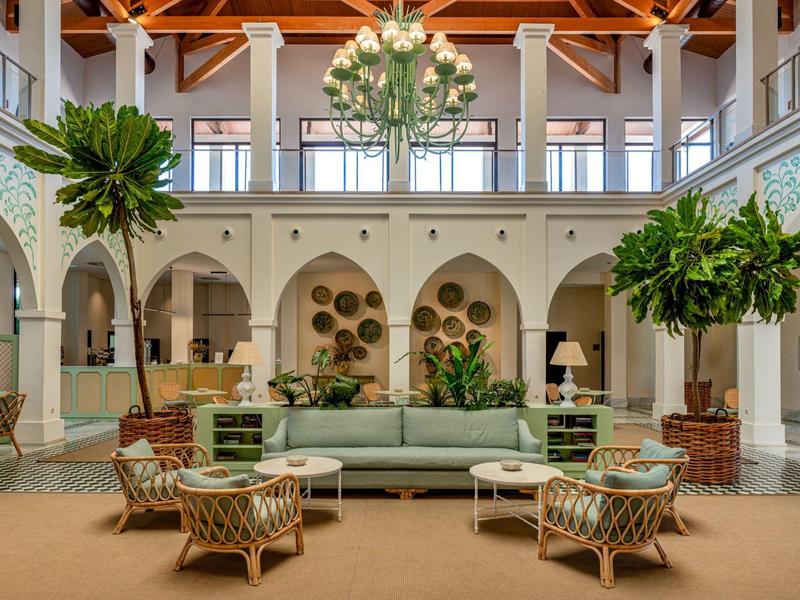 Helle Hotellobby mit hohen Holzbalkendecken, großen Pflanzen und elegantem Sitzbereich mit Sofas