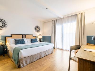 Helles Schlafzimmer mit großem Bett, Holzboden, Tisch mit Stuhl und lichtdurchflutetem Fenster.